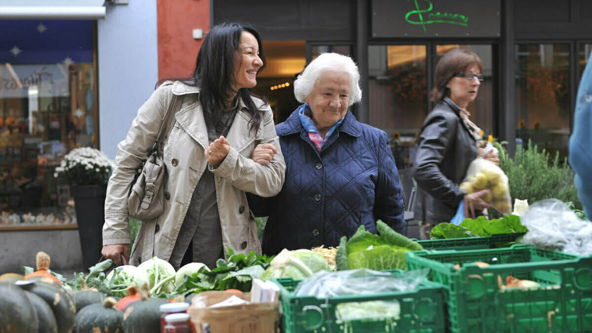 eine Rentnerin geniesst, dank der Unterstützung ihrer Begleitung, das Einkaufen auf dem Wochenmarkt