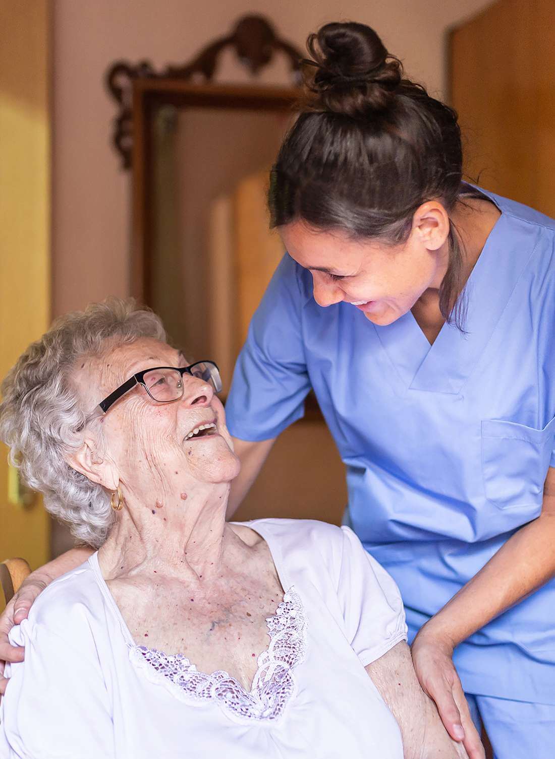 Fröhliche Seniorin lacht mit ihrer Pflegerin der Spitex Gäu in ihrem Zuhause.