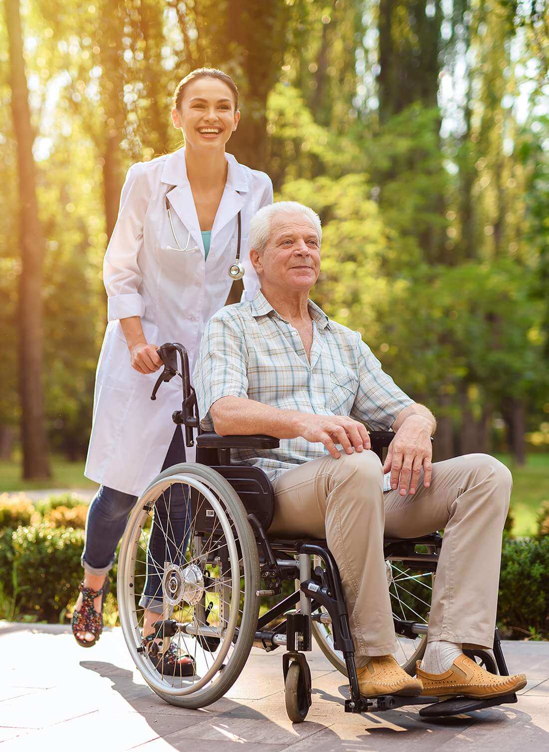 Betreuerin geht mit einem älteren Herr im Rollstuhl in einem sonnigen Park in Liestal spazieren.